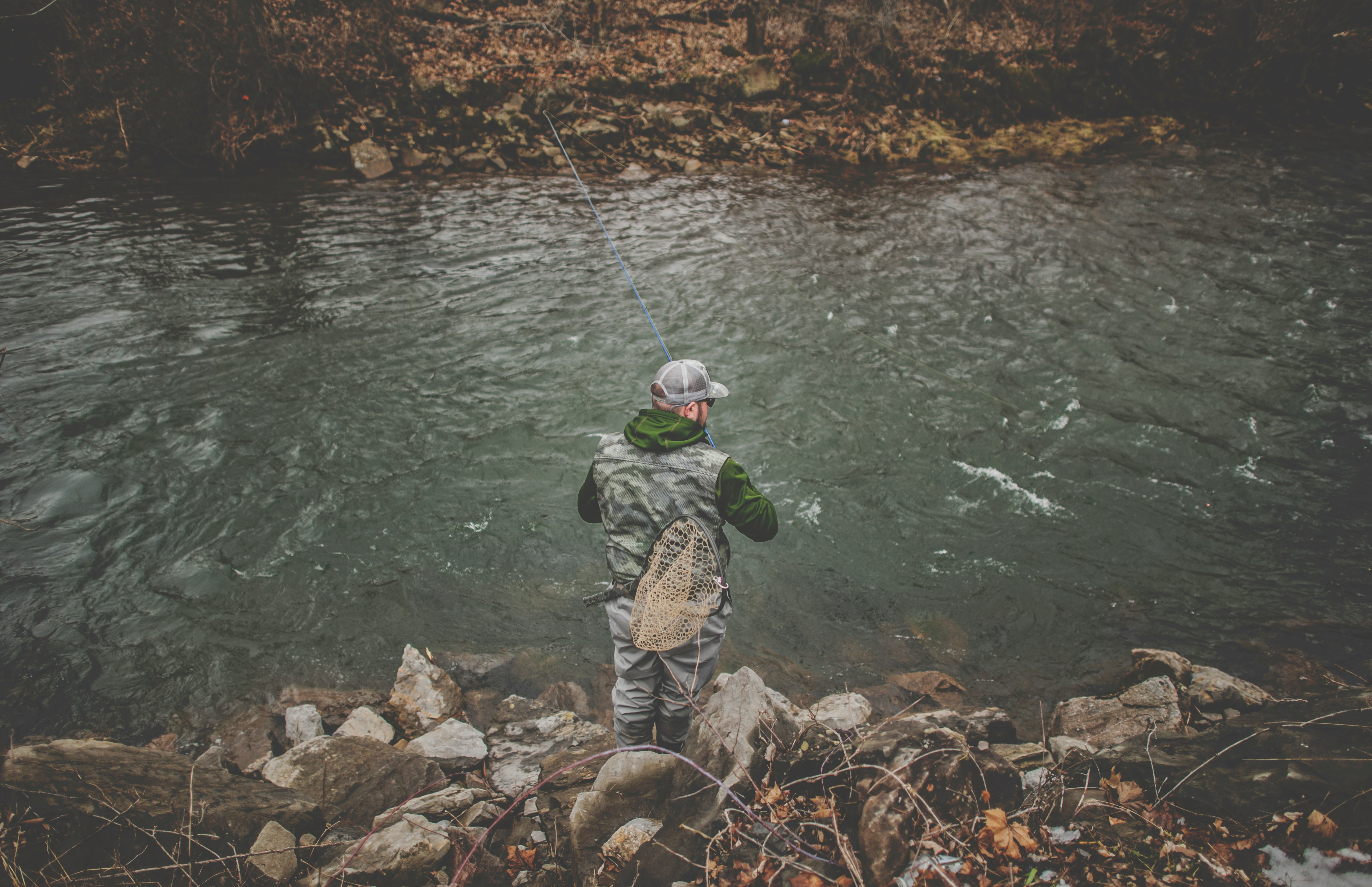 man in gray jacket and black pants fishing on river during daytime